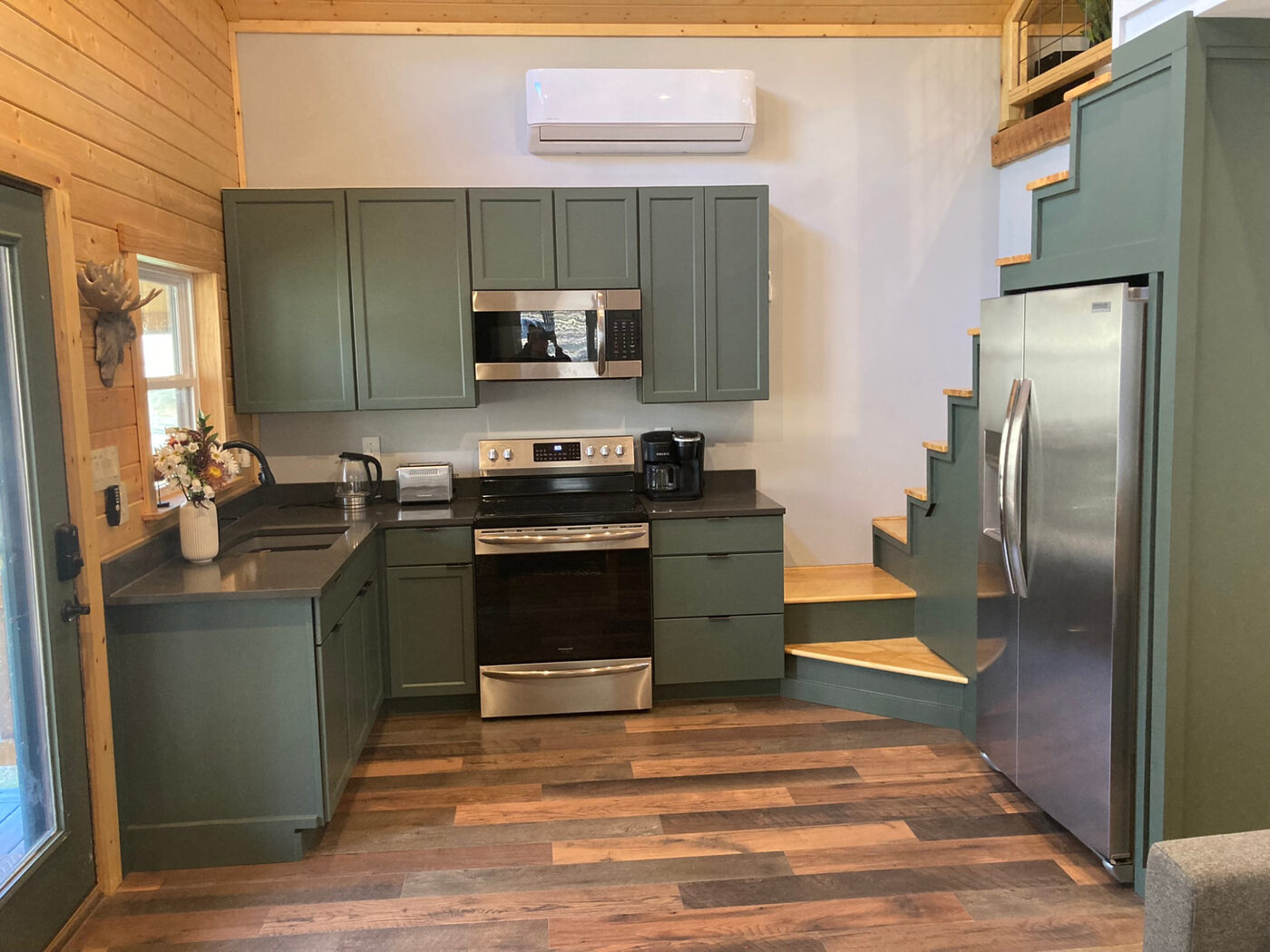 The kitchen with sage green cabinets and stairs built around the refrigerator