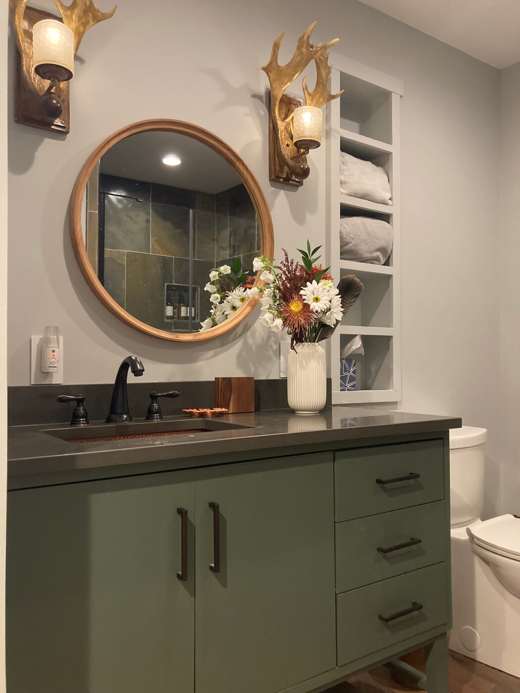 The bathroom vanity, a round wood mirror between two antler sconces