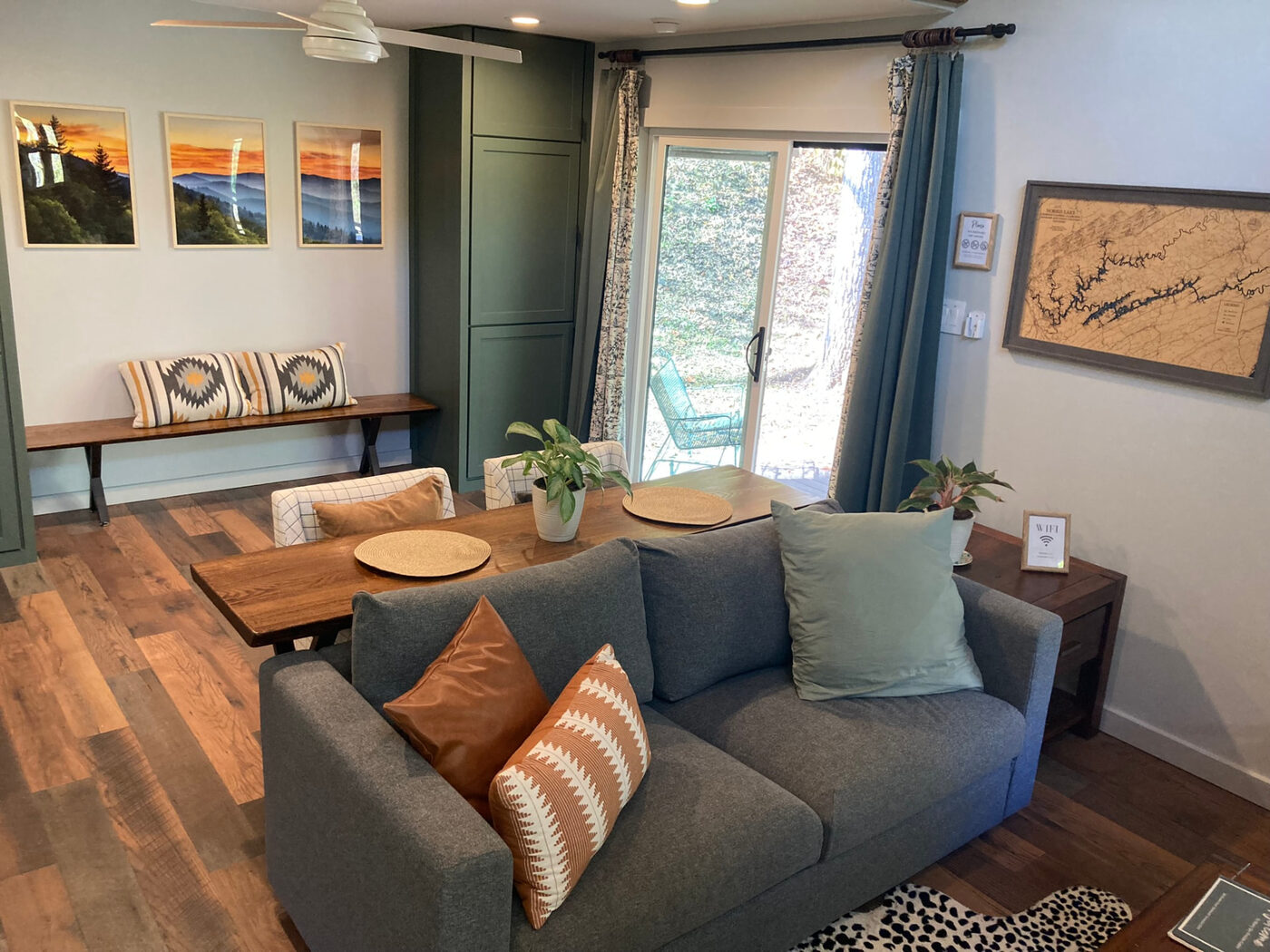 The living and dining space, with a grey sofa and windows onto the woods
