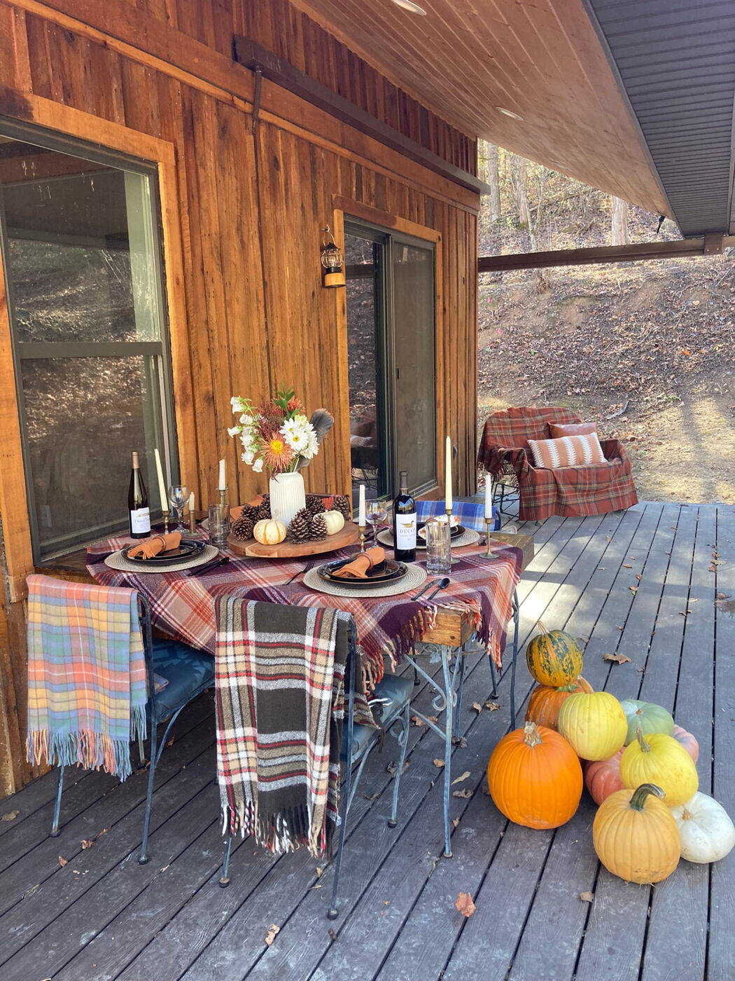 A deck table set for two, plaid blanket and pumpkins beside it